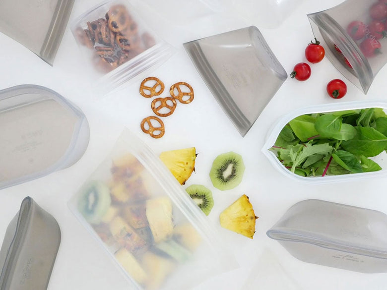 Zip Topジップトップディッシュのプラチナシリコーン製食品保存容器と蓋が、果物や野菜とともにトレイに整然と並べられているキッチン用品の写真