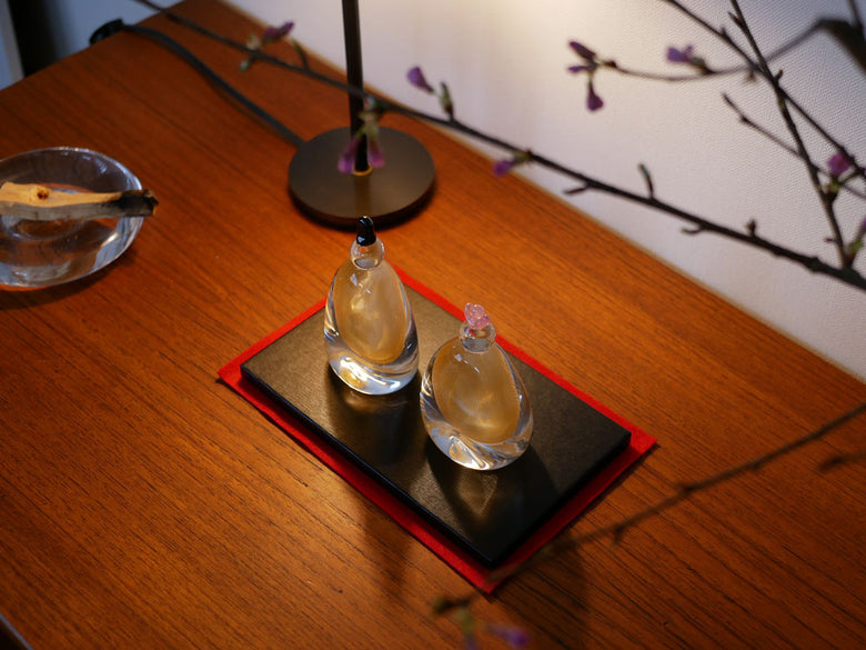 硝子屋PRATO PINOの手作りガラス製お雛様セット。お内裏さまとお雛さまが木箱と飾り台に並んで展示されています。