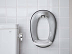 銀色のオーバル型フィルムフックがトイレ便座に取り付けられたバスルームの様子。洗練されたデザインで清潔感のある配管器具と調和しています。